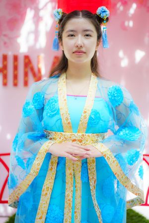A person wearing a traditional Chinese hanfu dress in light blue with gold trim and ornate hair accessories against a pink background.
