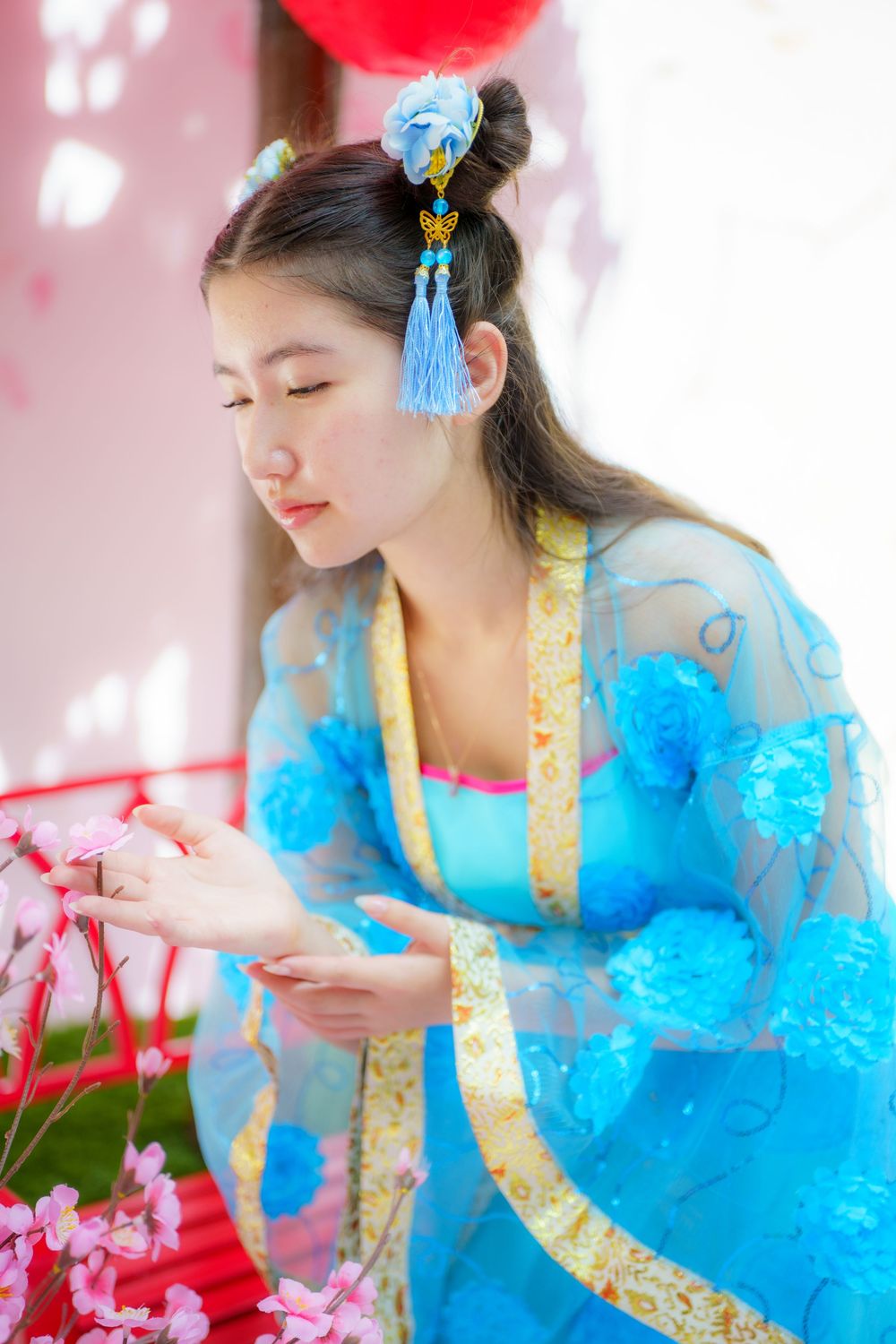 Traditional Chinese hanfu dress in bright blue with gold trim shown with pink cherry blossoms and ornate hair accessories.