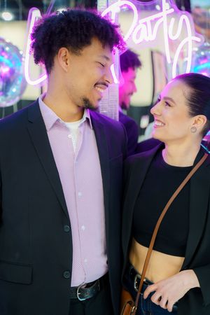 Couple sharing a joyful moment together under pink neon lights, dressed in formal and casual attire.