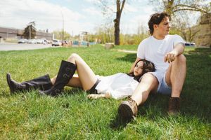 Two people relax on green grass in a sunny park while wearing casual clothing.