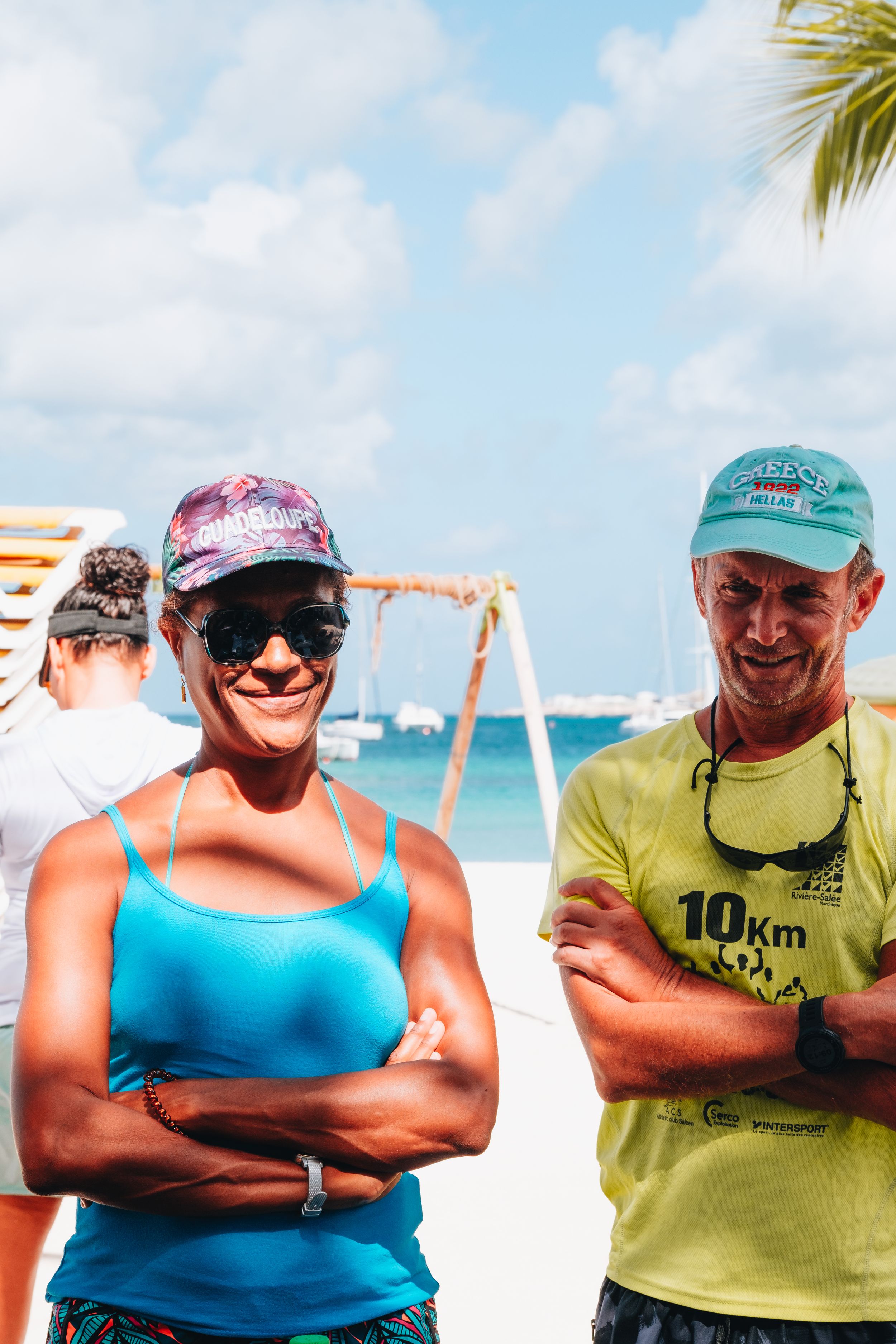 Athletes in athletic wear and hats pose together at a sunny beach with palm trees.