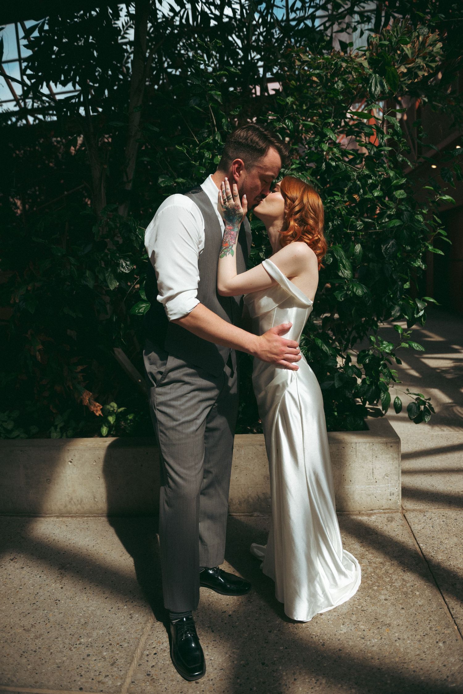 A romantic wedding couple sharing a kiss in dappled sunlight against a lush garden backdrop.