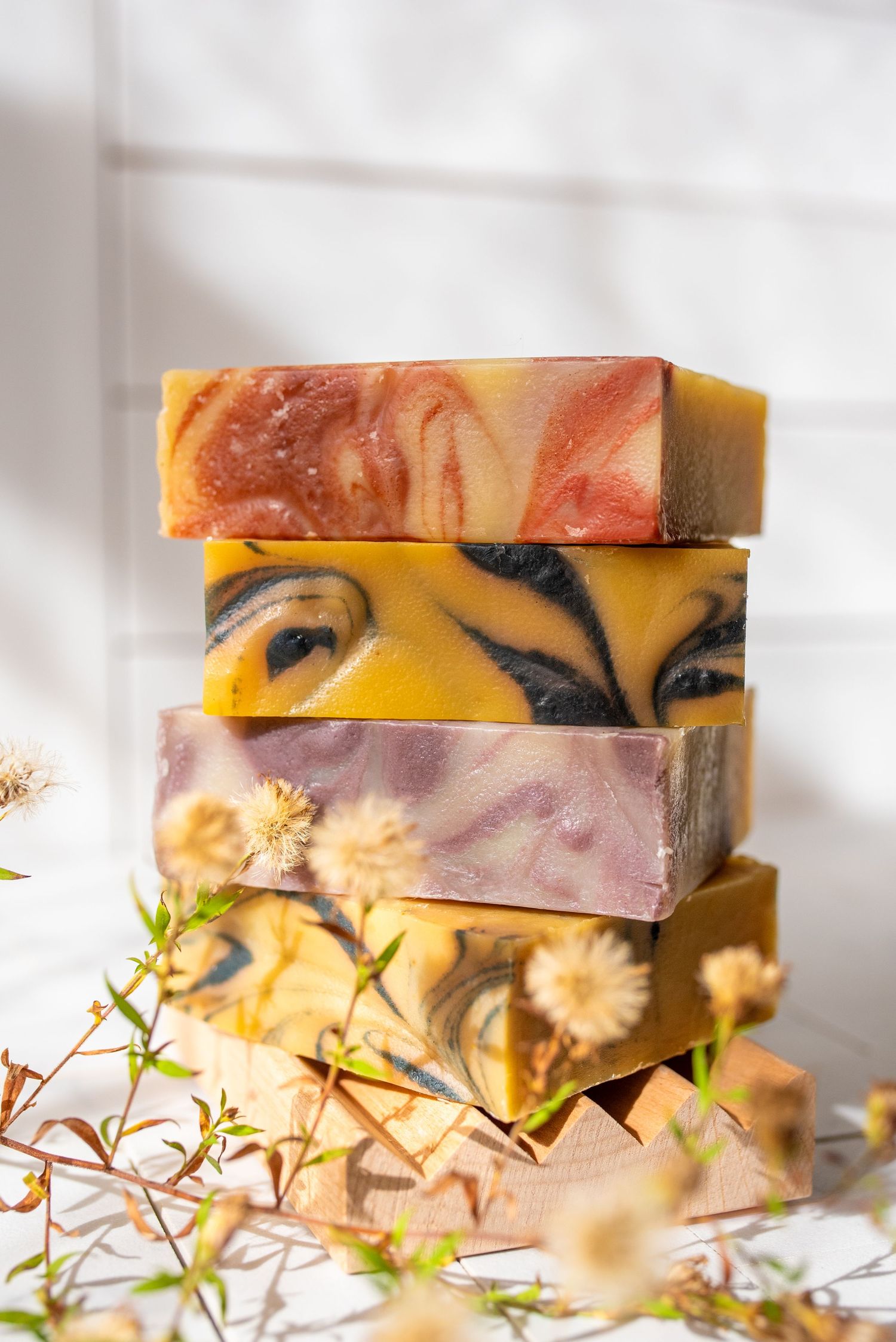 Stacked bars of handmade artisanal soap in yellow and pink marbled patterns with dried flowers.