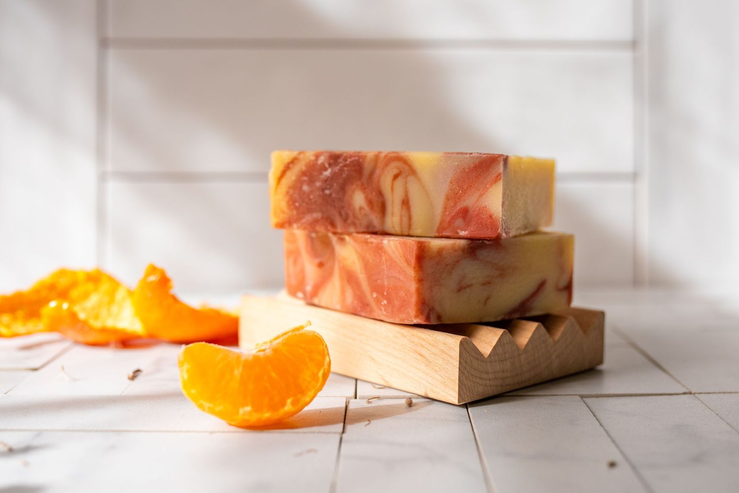Natural soap bars displayed with fresh oranges and decorative elements on white wood background.