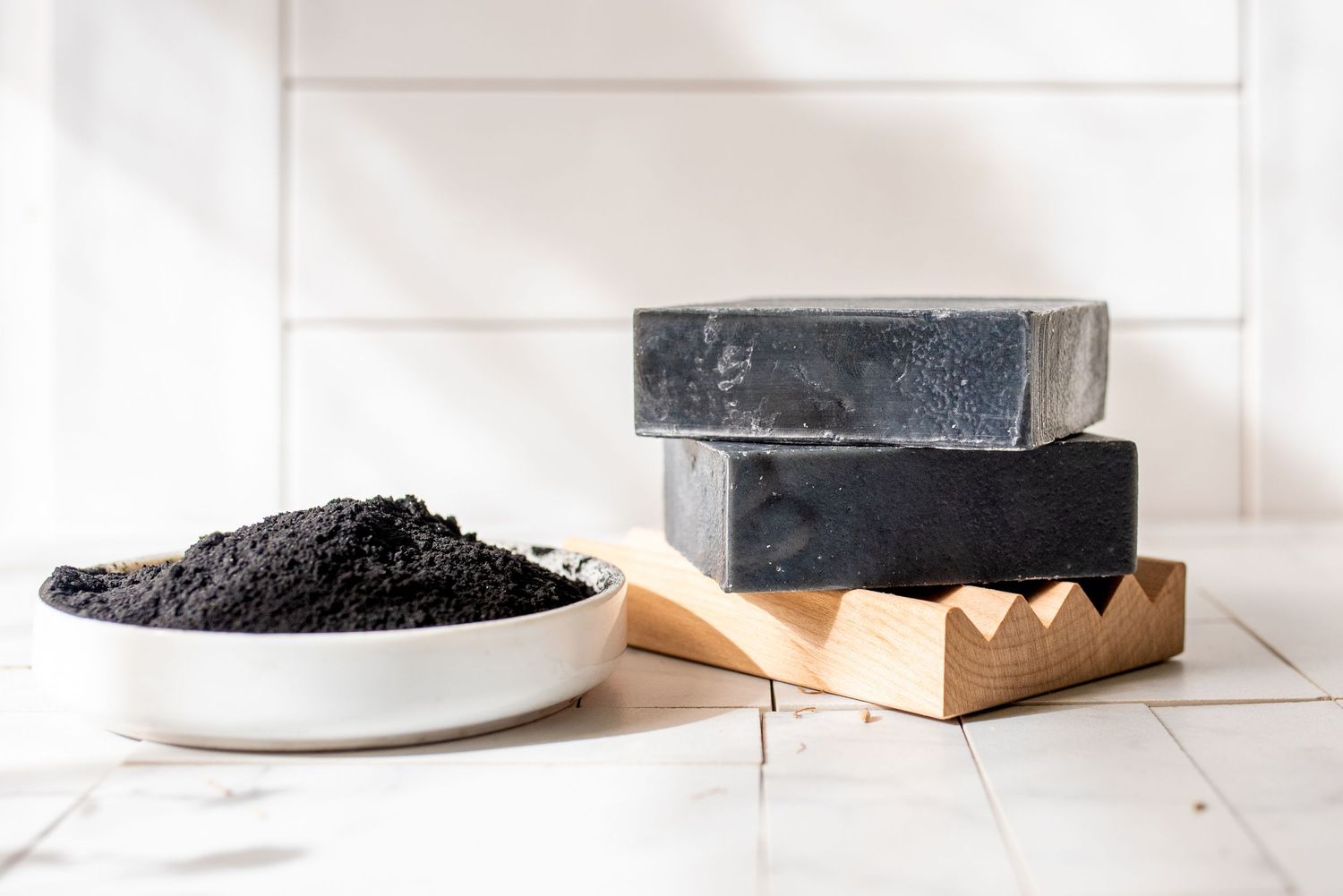 Charcoal colored handmade soap bars arranged on a white wooden surface.