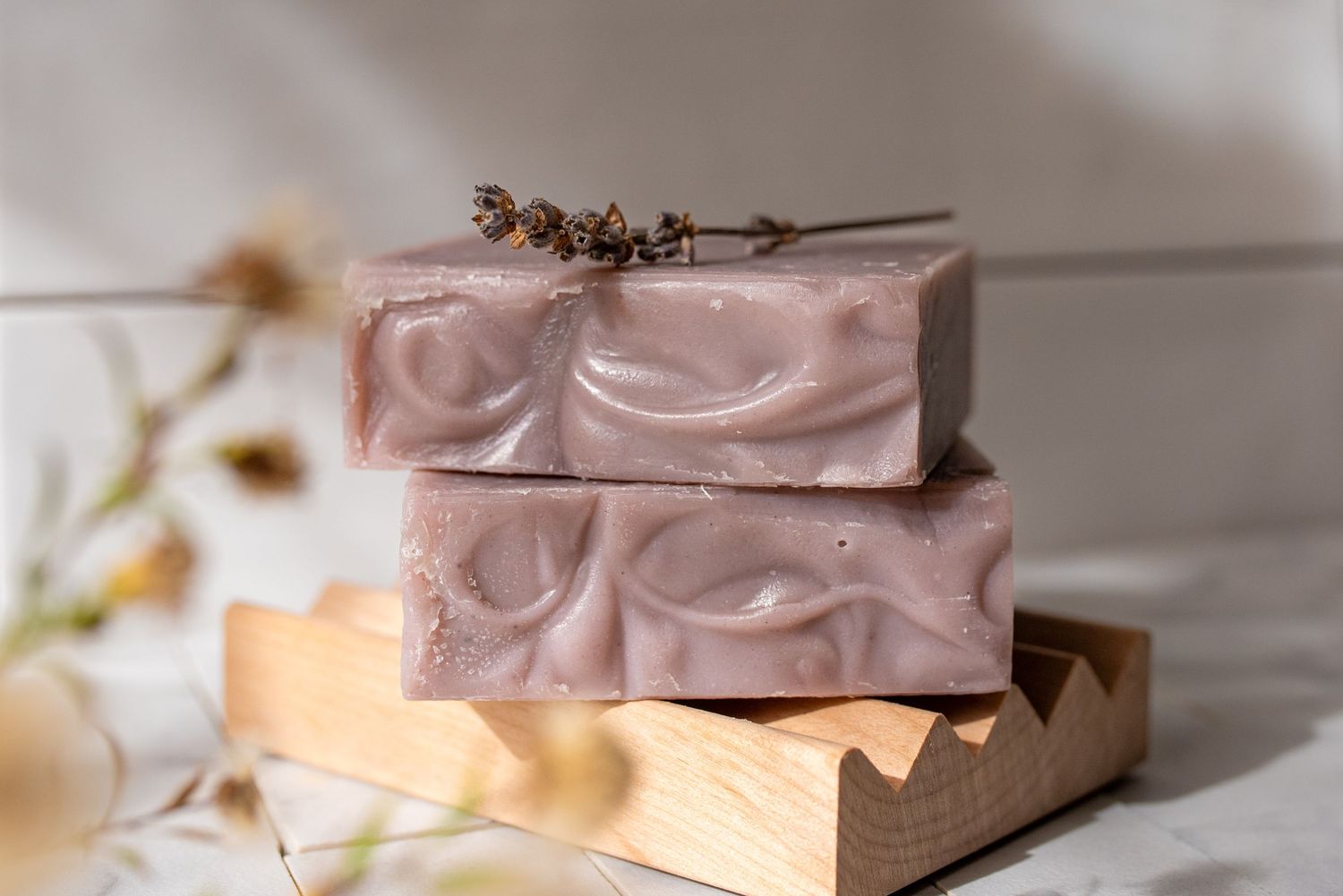 Pink and purple toned artisanal soap bars stacked on wooden surface with natural lighting.