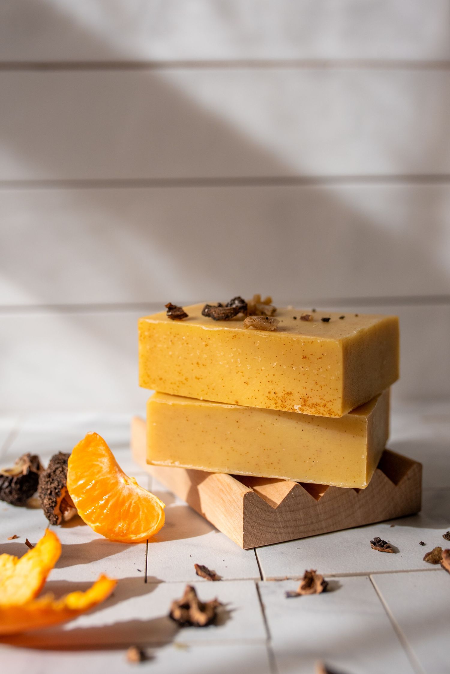 Yellow handmade soap bars with orange slices and spices on rustic white wooden background.