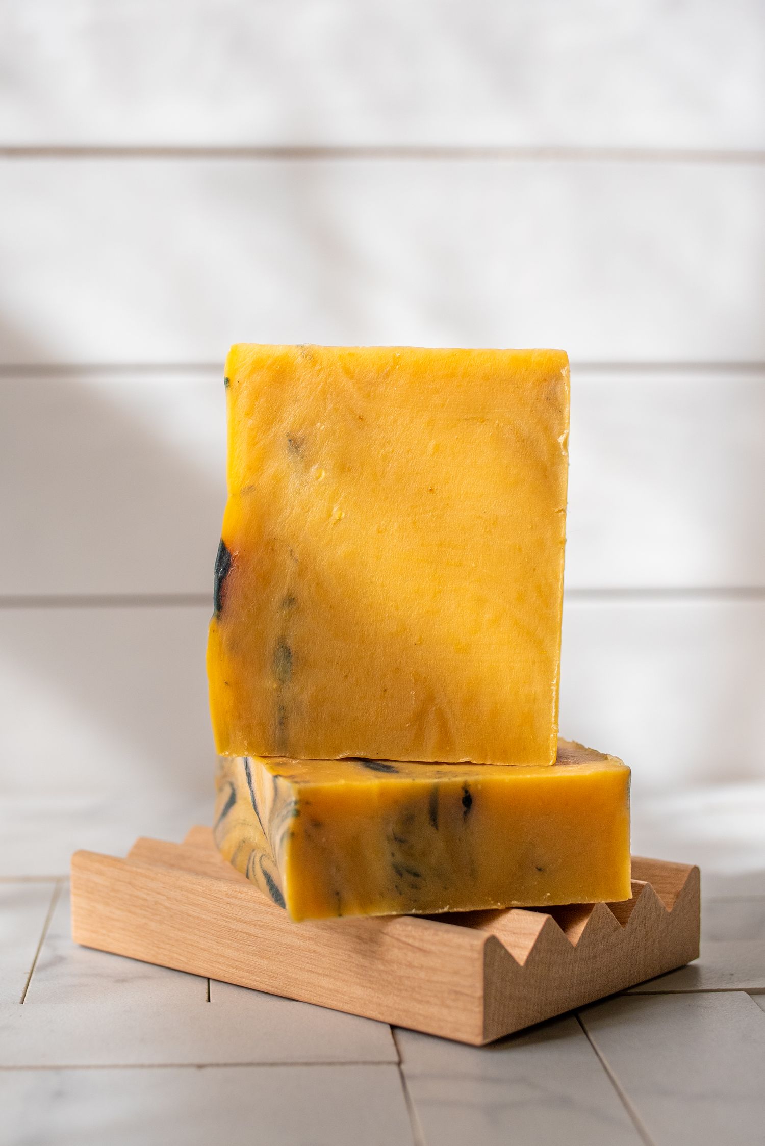Yellow handmade soap bars with swirled pattern on wooden soap dish.