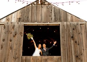Newlyweds celebrate in rustic barn window with string lights.