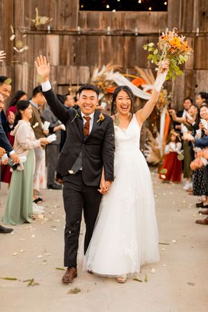 Newlyweds celebrate with joyful recessional in rustic barn venue.