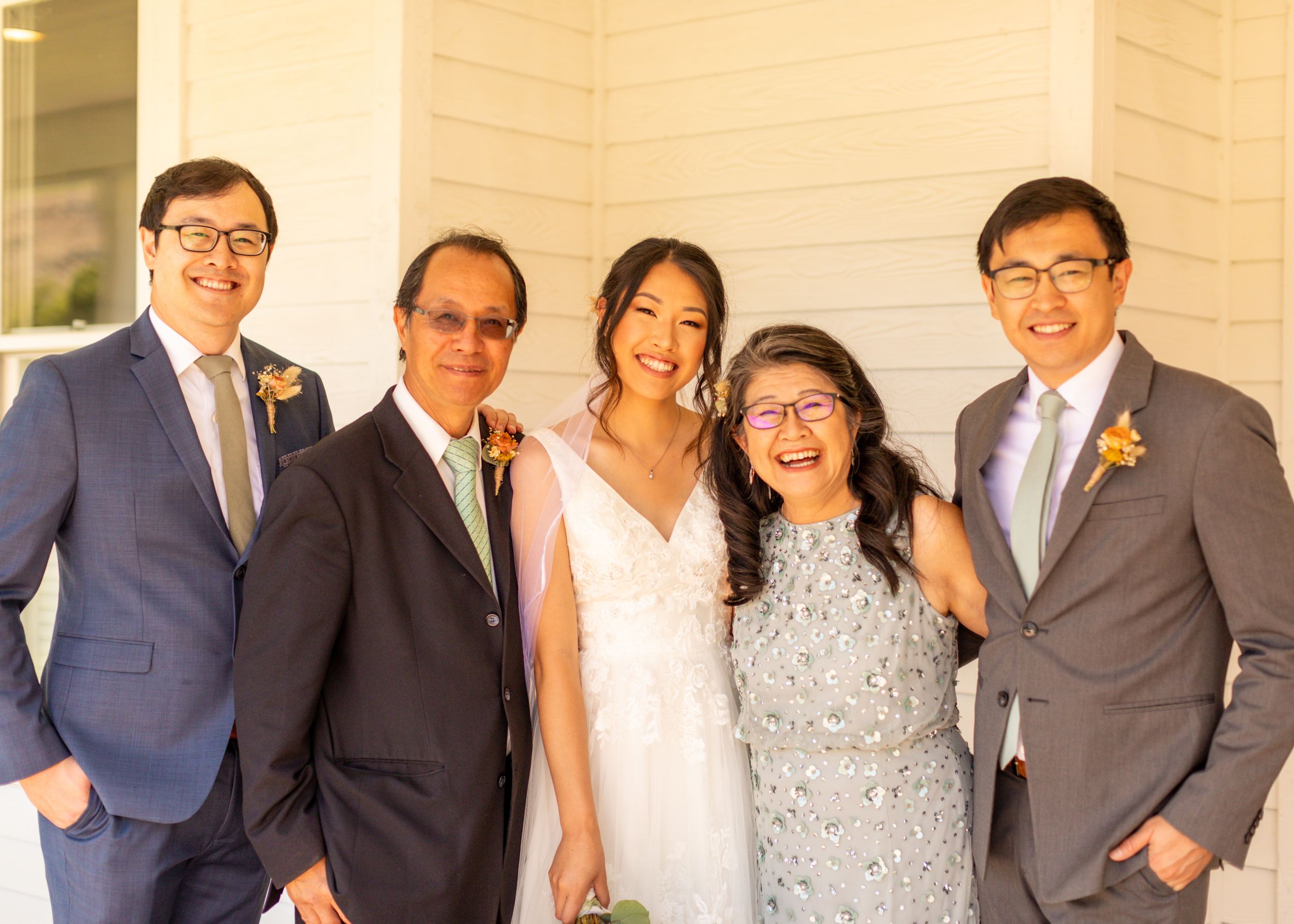 Wedding party poses together in formal attire on porch.
