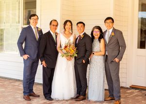 Wedding party dressed in formal attire poses together on white porch.
