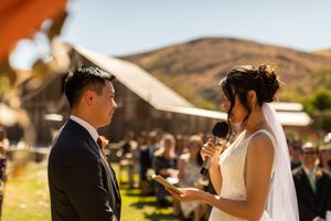 Couple exchanging vows during outdoor ceremony with rustic barn backdrop.