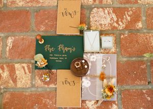 Wedding invitation suite featuring floral designs and gold details on brick texture.
