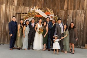 Wedding party in formal attire poses in front of rustic wooden barn.