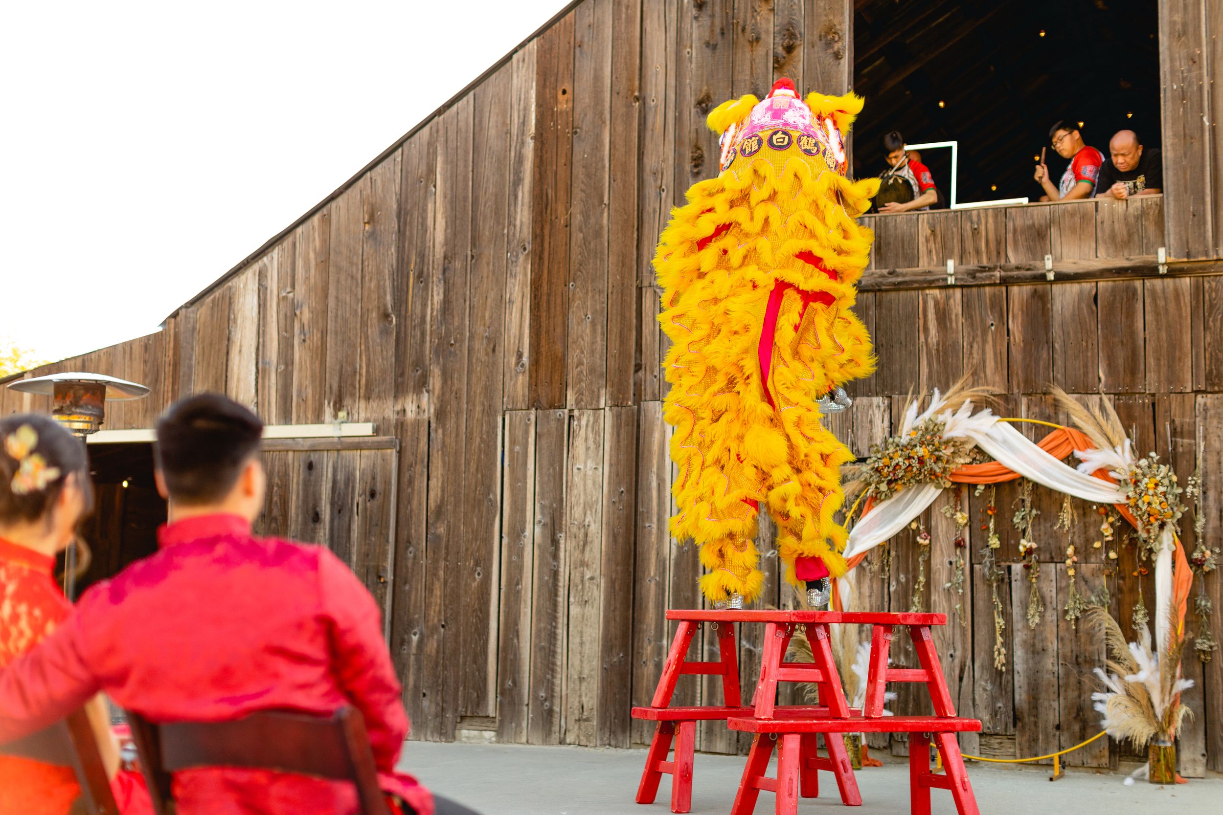 Lion dance performers entertaining wedding guests from rustic barn doorway.