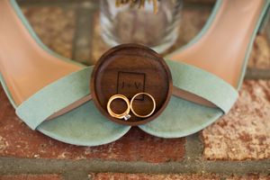 Wedding rings displayed on a rustic wooden holder with mint green shoes in the background.
