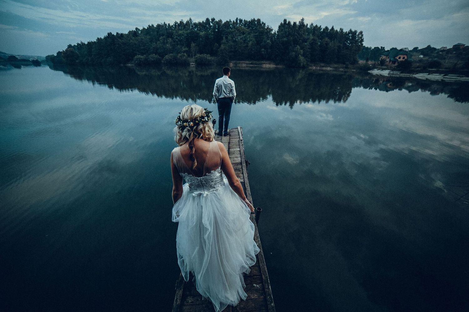 Couple in wedding attire holding hands while standing in front of a majestic waterfall surrounded by lush greenery.