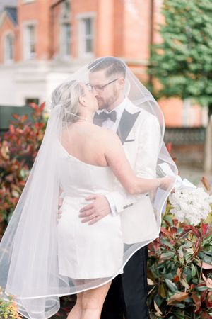 Bride and groom sharing a kiss under the bridal veil in The Park Estate near Nottingham Castle, framed by soft light and old brick walls.