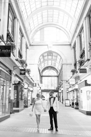 Wide shot of bride and groom holding hands under the large arched windows inside Nottingham Council House on their wedding day.