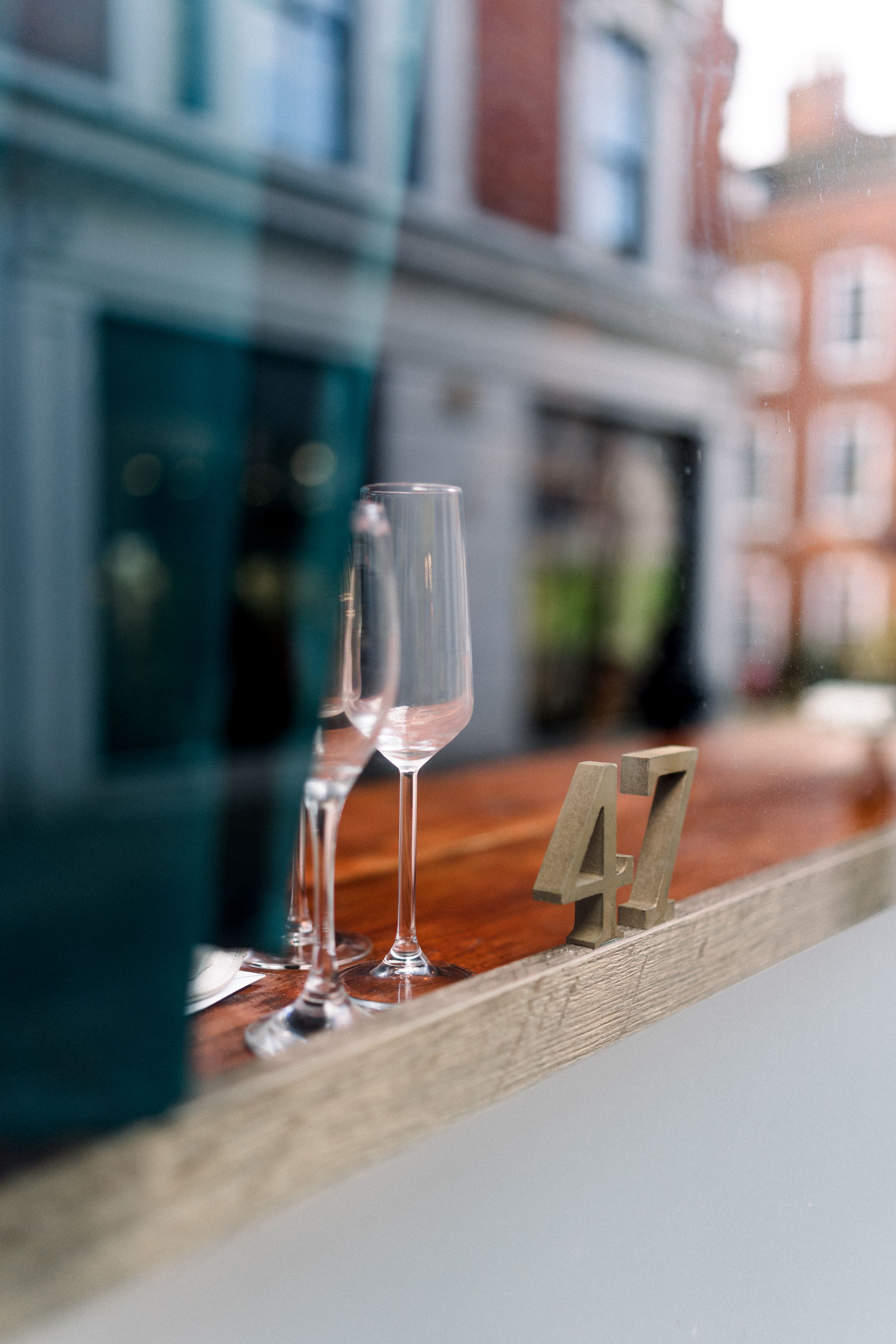 Creative shot of champagne glasses behind a window with the ‘47’ sign and Nottingham city buildings reflecting in the glass.