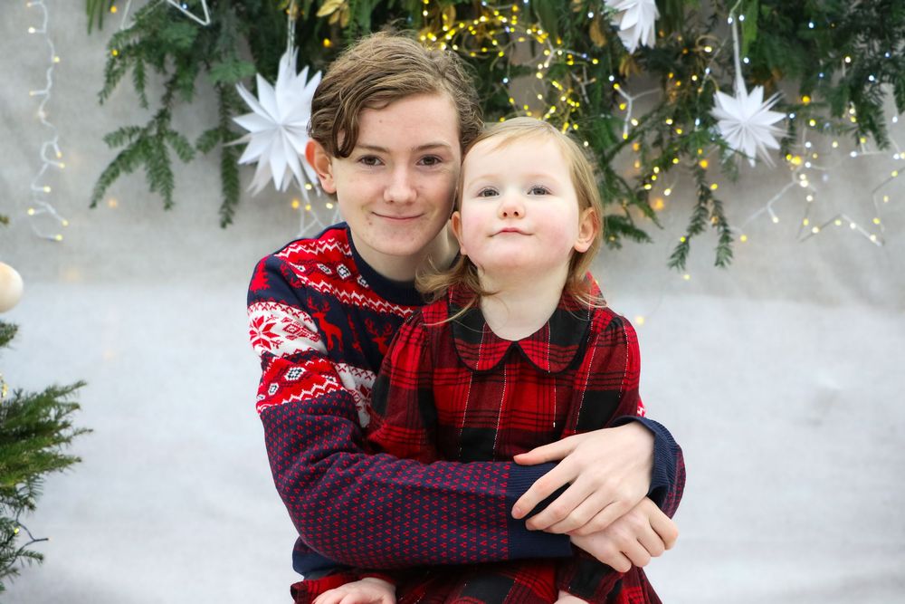 Holiday portrait with festive sweaters against Christmas tree backdrop with white star decorations.