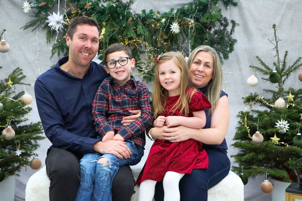 Family poses together for holiday portrait with decorated Christmas trees and white star ornaments.