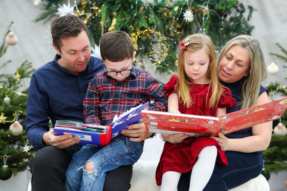 Family reads holiday stories together while sitting by decorated Christmas tree.
