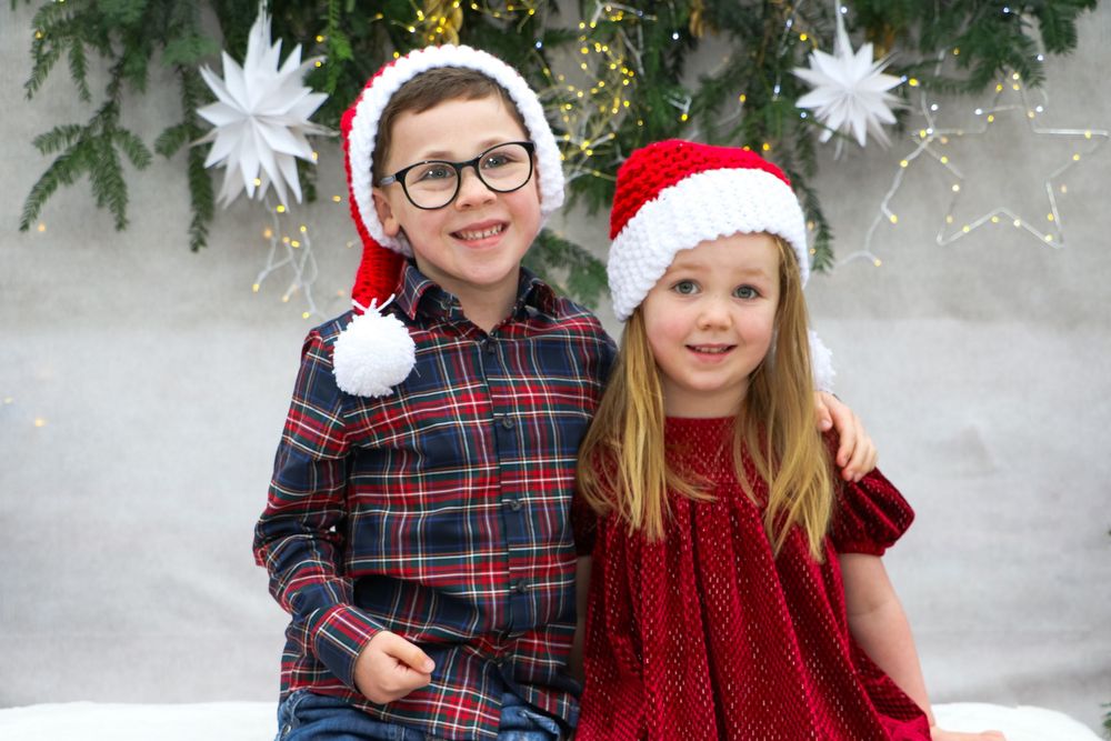 Holiday portrait with plaid shirts and Santa hats against Christmas tree backdrop.