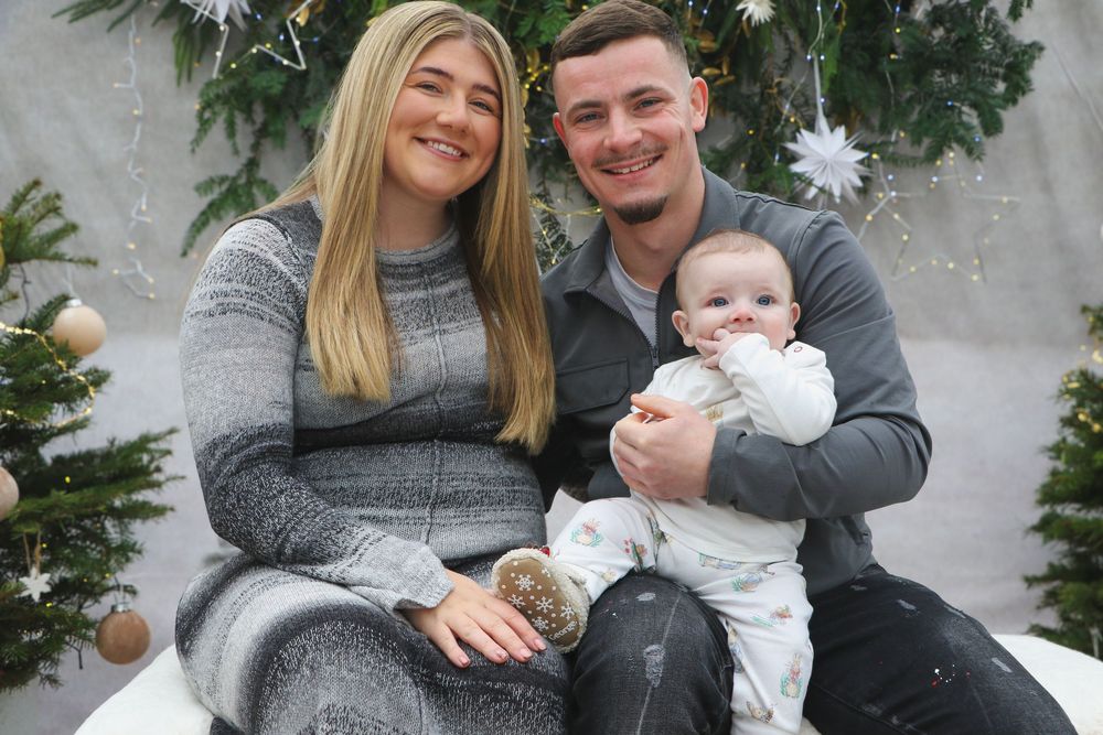 Holiday portrait in front of decorated evergreen branches with twinkling lights and ornaments.