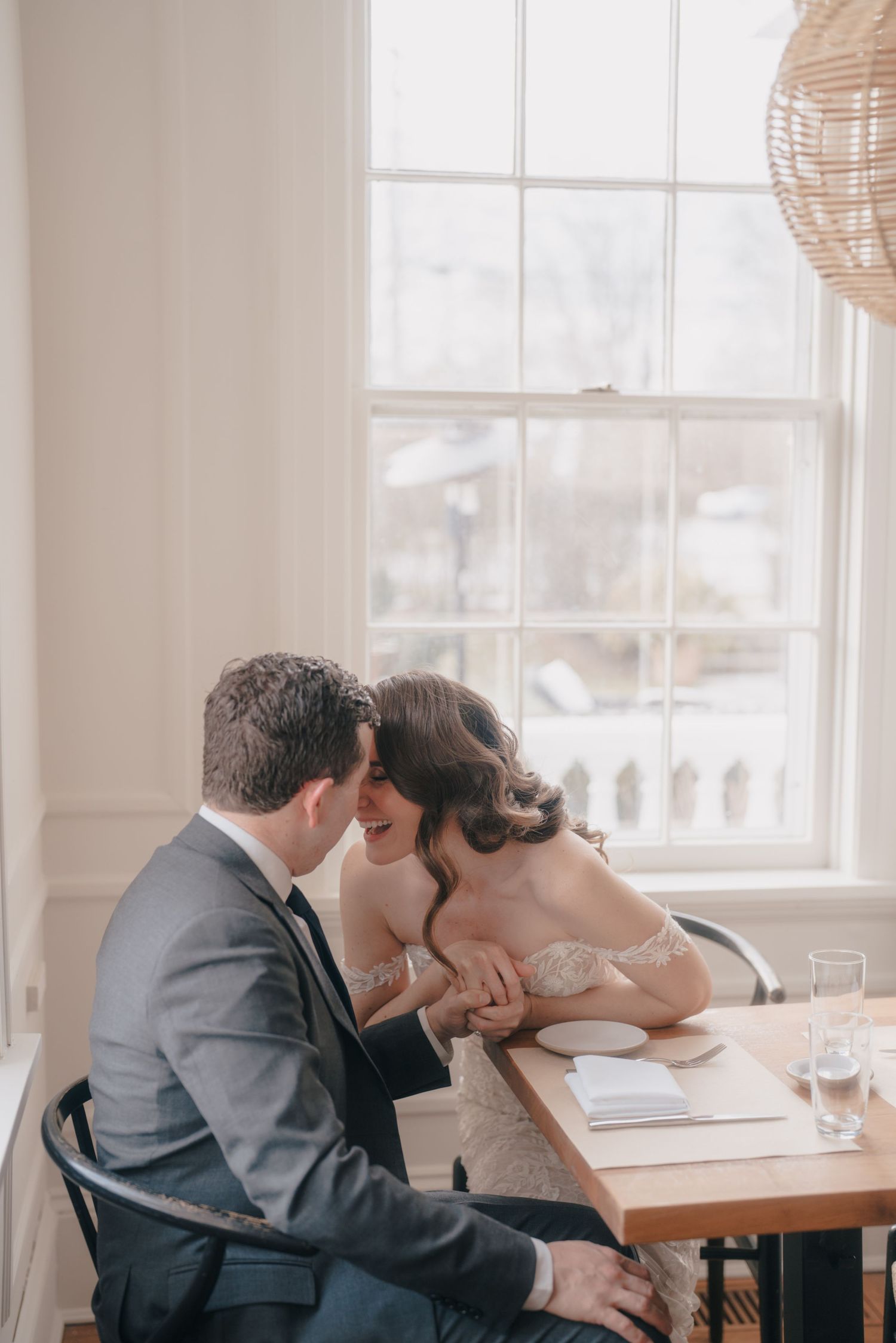 Intimate moment shared at a dining table by window in soft natural light.