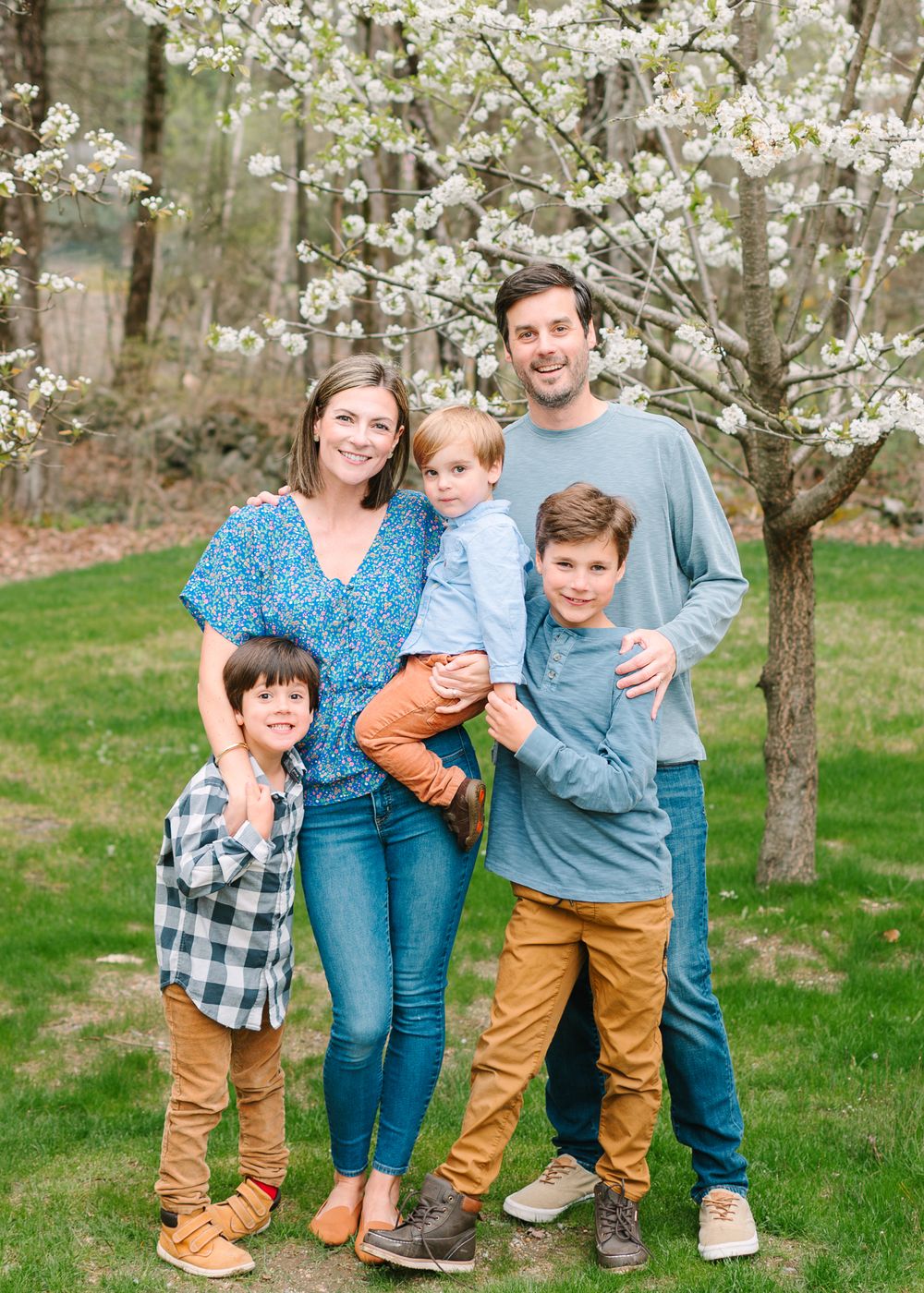 Family poses together in front of blooming white cherry blossom tree on green spring lawn.