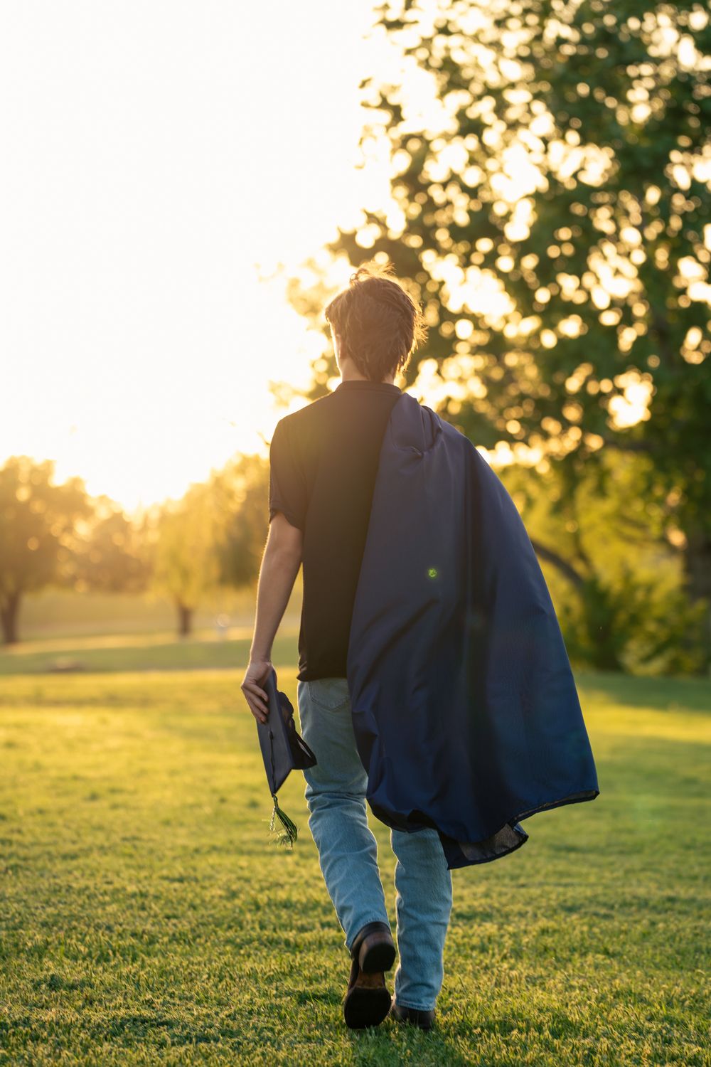 Silhouettes of a person walking on grass at sunset with golden sunlight filtering through trees.