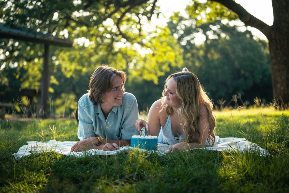 A couple lying on a blanket in a grassy field at sunset during a romantic picnic date.