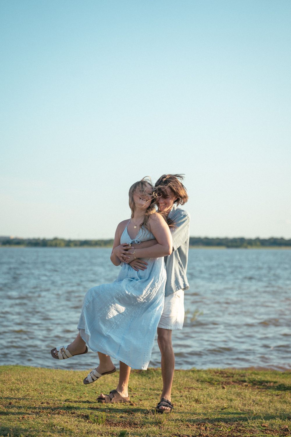 A romantic couple dances together on grassy shoreline at sunset with ocean waters in the background.