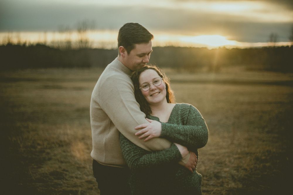 A loving couple embraces in a golden field at sunset while wearing cozy sweaters on a peaceful evening Edmonton Engagement Photographer