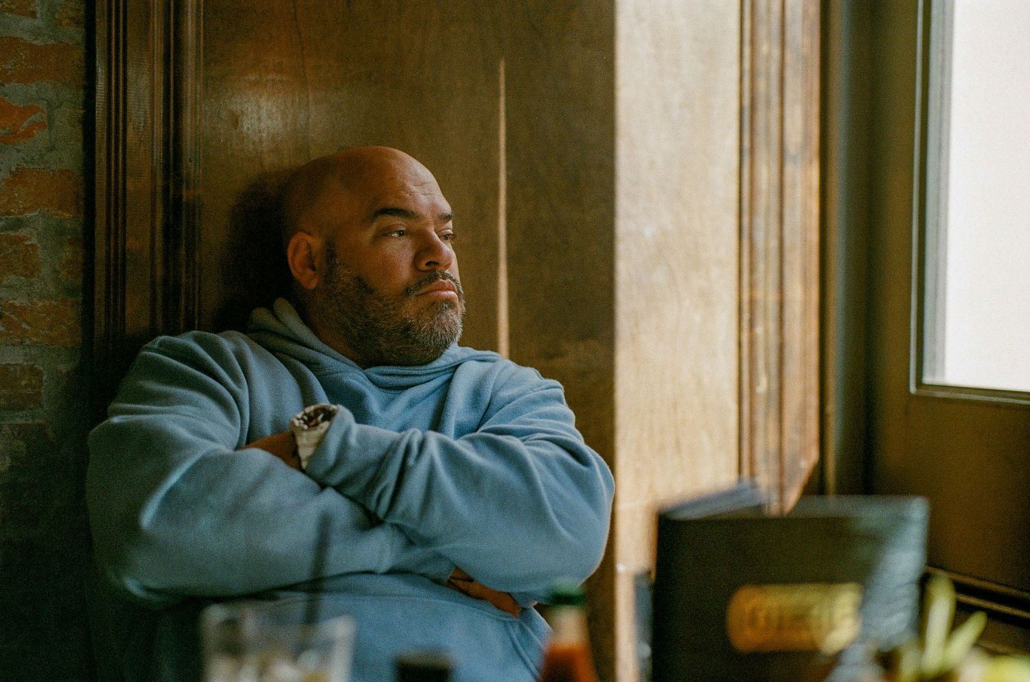 A person in a light blue sweater gazes thoughtfully out a window while seated in a restaurant.