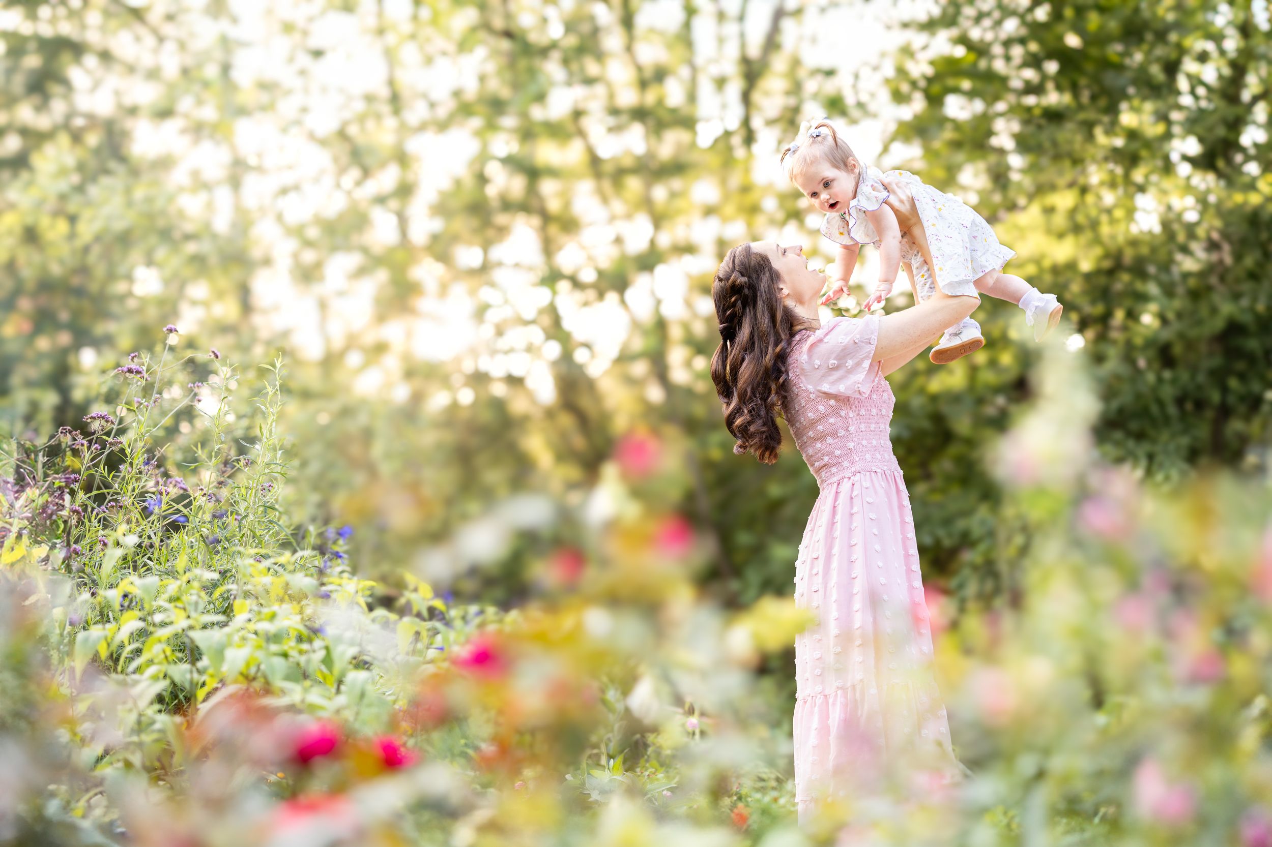 Photograph of mom holding a baby with dreamy glowing backlight and beautiful floral surroundings at Williamsburg Botanical Garden.