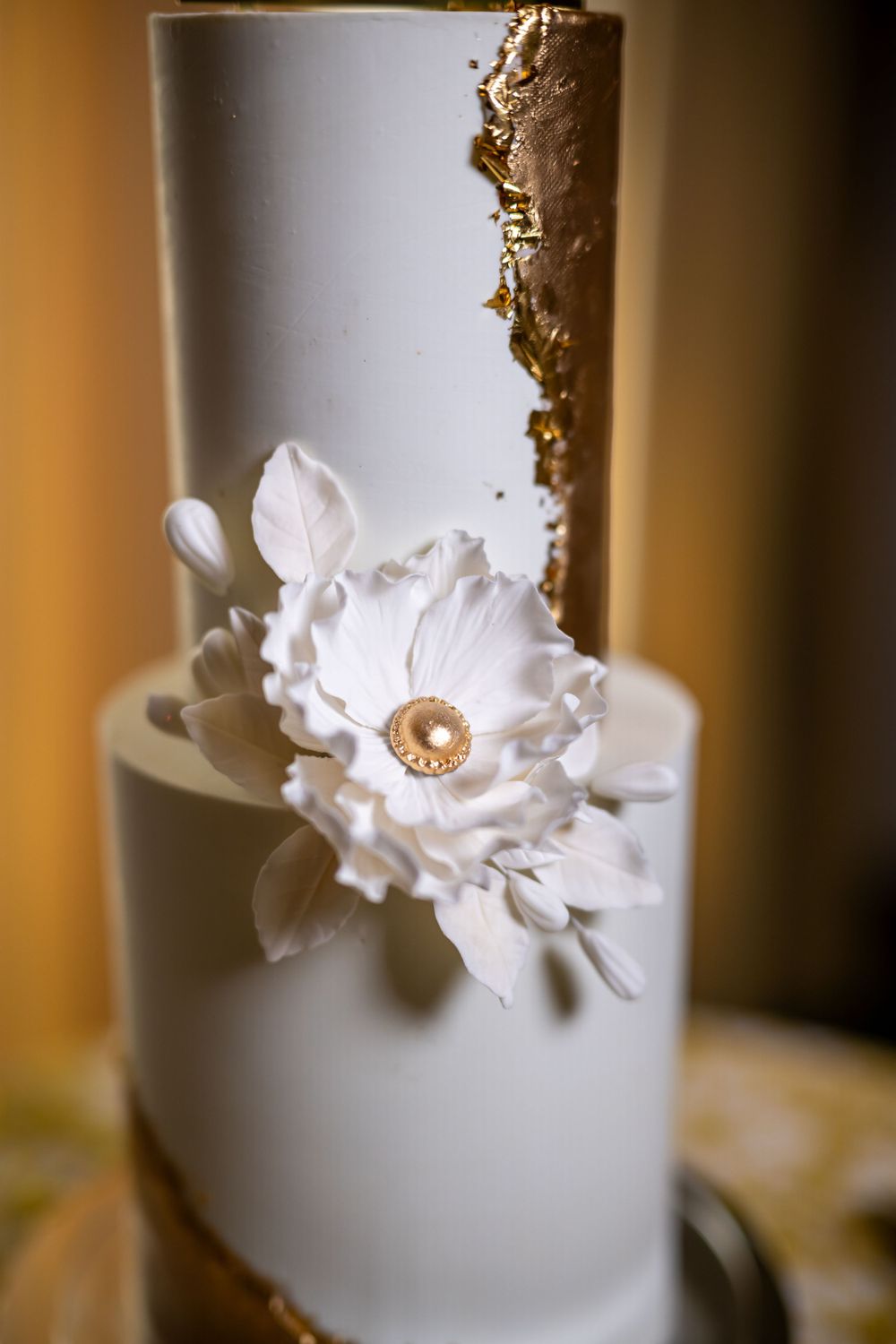 Close-up of a white wedding cake with gold accents and handcrafted sugar flower details.