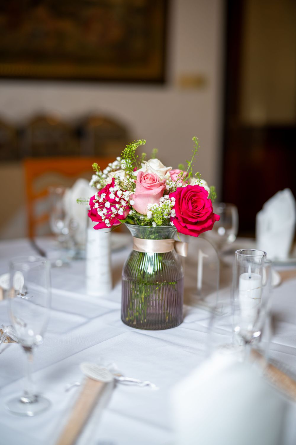 Pink roses and baby's breath centerpiece in a purple mason jar on white tablecloth.