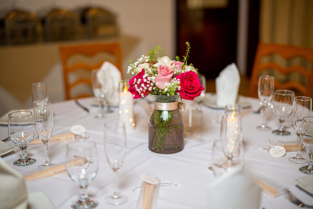 Wedding reception table set with floral centerpiece featuring pink roses in vintage mason jar.