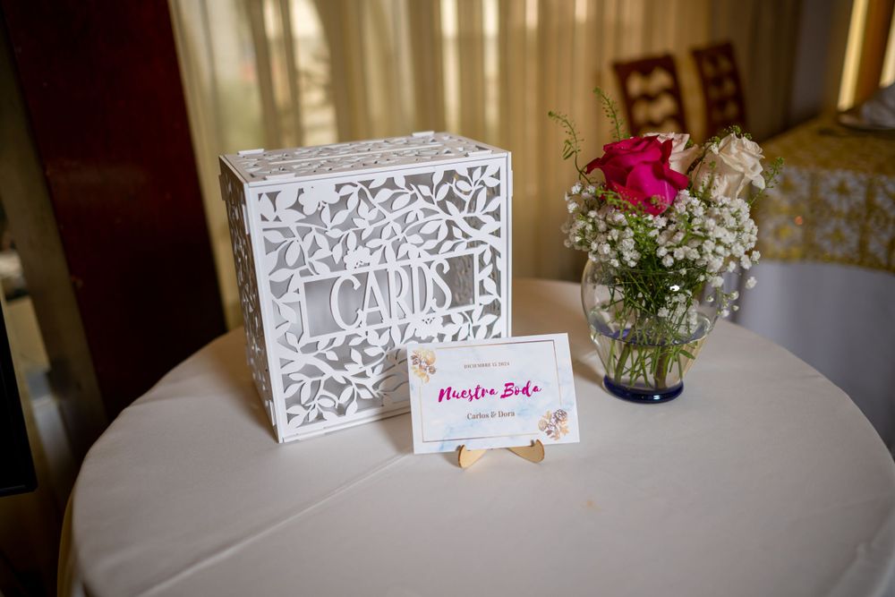 White decorative card box and place card with pink flower vase on round table.
