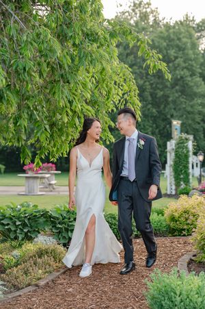 A bride and groom walk along a pathway with trees and flowers at their wedding at Post Family Farm