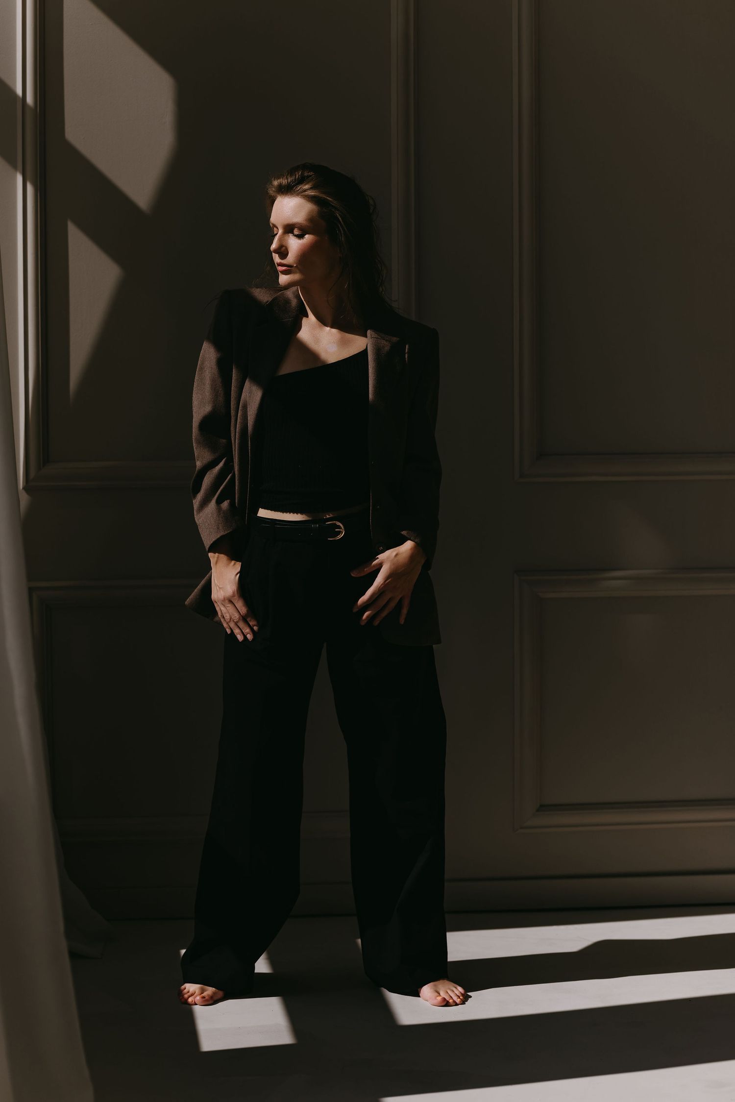 Dramatic portrait in black outfit with sunlight casting shadows through window.