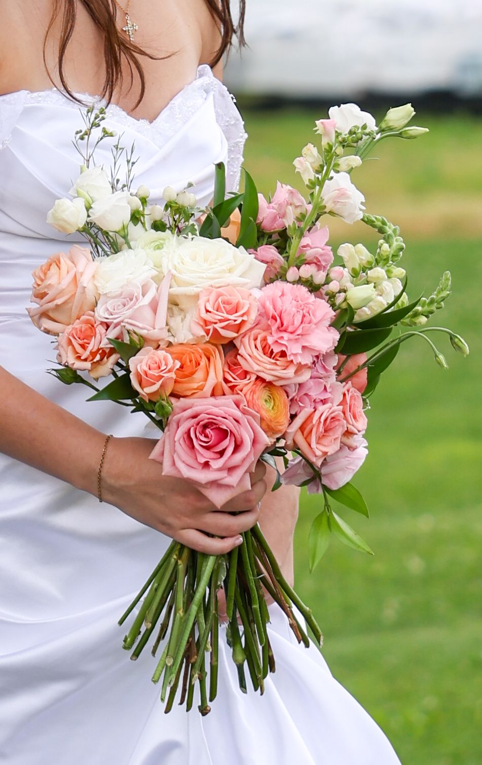 Bride holds stunning pink, peach, and white rose wedding bouquet in front of white gown.
