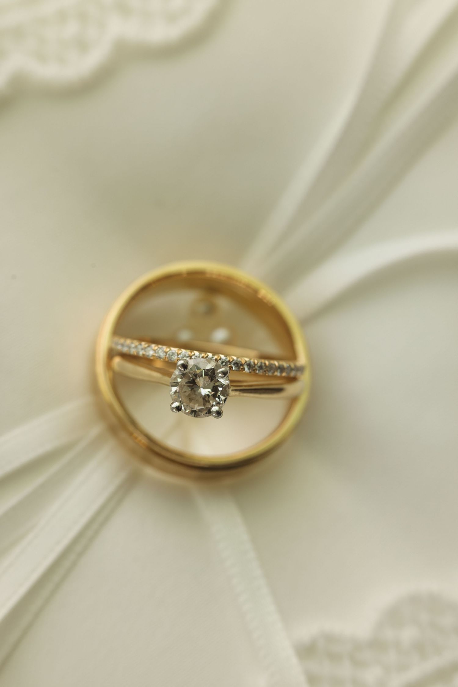 Gold diamond engagement ring and wedding band displayed on white lace bridal fabric.