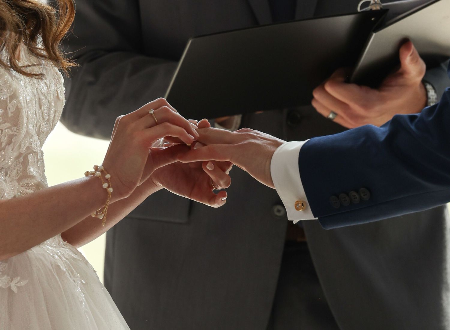 Groom placing wedding ring on brides finger during outdoor wedding ceremony.