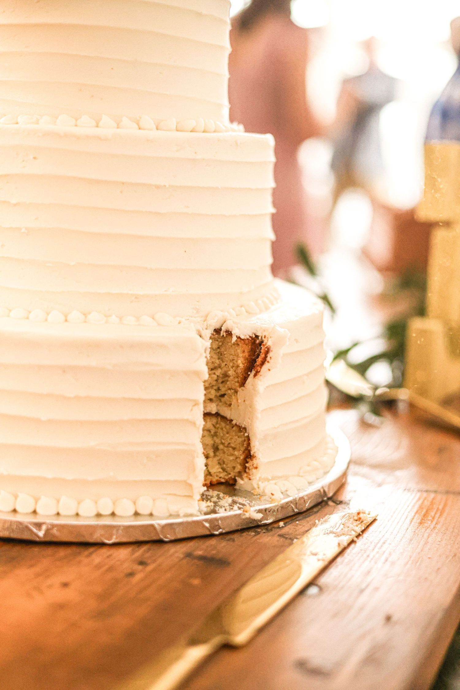 Elegant white tiered wedding cake with a slice cut out on a rustic wooden table.
