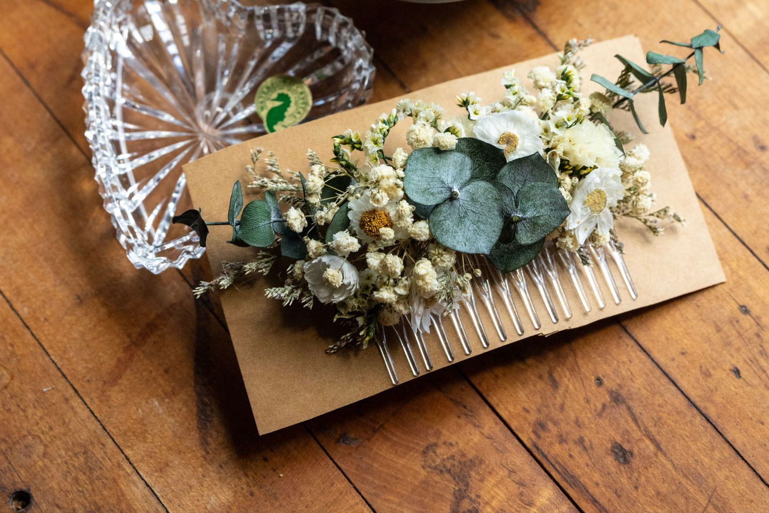 Elegant bridal hair comb adorned with dried eucalyptus, white flowers, and greenery on kraft paper background.