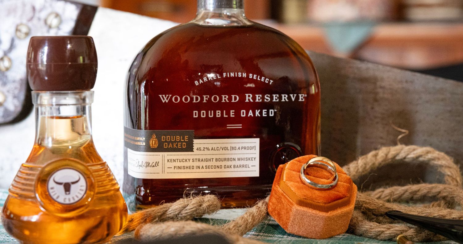 Woodford Reserve Double Oaked bourbon bottle displayed with wedding ring on orange ribbon and decorative rope.